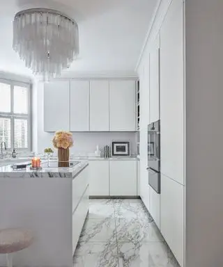 Cuisine blanche élégante avec lustre en verre, sol en marbre, armoires blanches et îlot de cuisine, tabouret tulipe rembourré