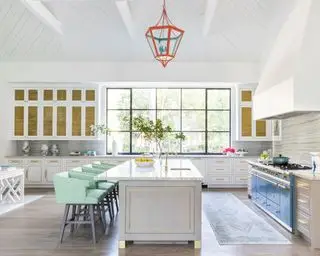 Grande cuisine avec plafond lambrissé en bois blanc, suspension orange en métal et verre, grand îlot de cuisine avec sièges, tapis au sol entre l'îlot et la cuisinière, murs peints en blanc, armoires grises