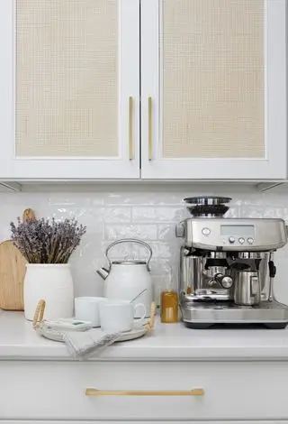 nærbilde av hvitt kjøkken med glasserte hvite bakplater hvite veggskap med rotte foran og hvitt og sølv tilbehør på benkeplaten