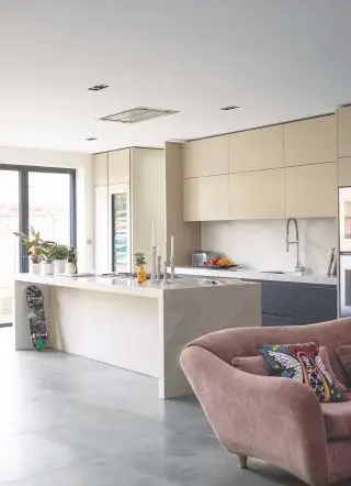 Cuisine avec sol en béton poli, îlot, armoires en bois et peintes et canapé au-delà