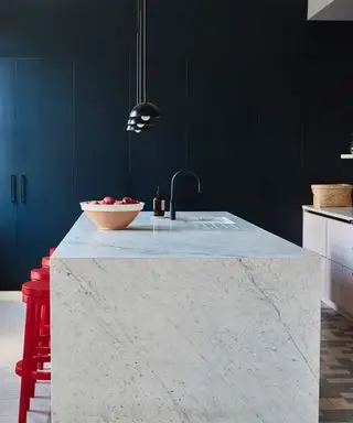 ¿Se puede colocar una isla en una cocina de galera? Isla de mármol, estilo galera, gabinetes azul marino del piso al techo, taburetes rojos.