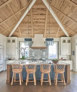 Duża kuchnia w nowym budynku z dużą niebieską wyspą kuchenną i wysokim sufitem pokrytym drewnem cyprysowym