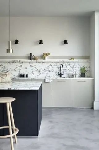 Surface de travail et dosseret de cuisine en marbre blanc dans un décor blanc avec îlot de cuisine peint en bleu nuit.