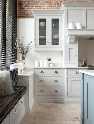 Cuisine blanche avec des éléments de bleu et de gris, des briques apparentes et des armoires de style shaker. mur