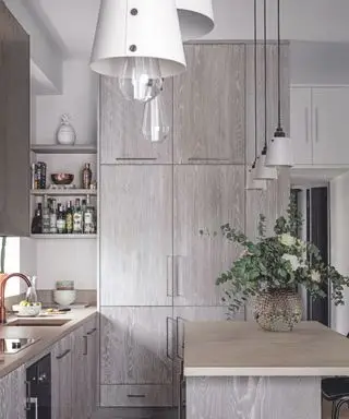 淡い灰色の木製キャビネット、木製の床、アイランド キッチンと白い壁の上に白いランプを備えたキッチン ダイナー