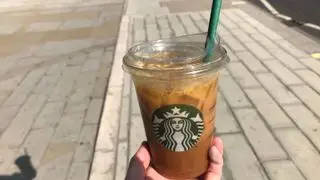 Café con aceite de oliva en una taza de Starbucks que se retiene en una calle luminosa