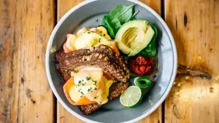 Un bol de desayuno con aguacate, huevos, salmón, lima y hojas en su interior.