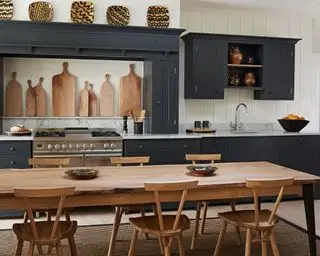 Cuisine gris foncé avec table et chaises en bois et une sélection de planches à découper en bois exposées.