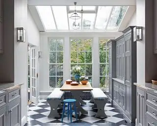 Une extension de cuisine grise avec puits de lumière, carrelage noir et blanc et rangements intégrés.