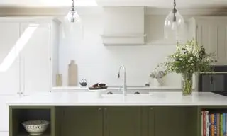 녹색으로 칠해진 주방 아일랜드, 흰색 캐비닛, 주방 아일랜드의 싱크대, 유리 펜던트가 있는 녹색 및 흰색 주방