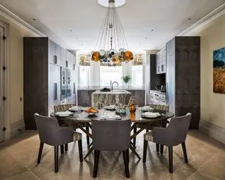 ダイニングエリアからキッチンへの眺め、円形テーブルの上のドラマチックな中央ライト、タイル張りの床、中央のキッチンアイランド。