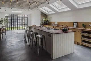 Un îlot de cuisine lambrissé en bois avec des tabourets de bar en métal rustique et des guirlandes lumineuses dans le salon.
