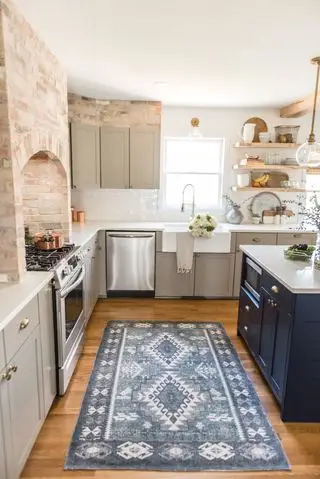 木製の床とむき出しのレンガの壁を備えた素朴なキッチンに、淡いストーン グレーとミッドナイト ブルーでペイントしたキッチン キャビネットのアイデア。