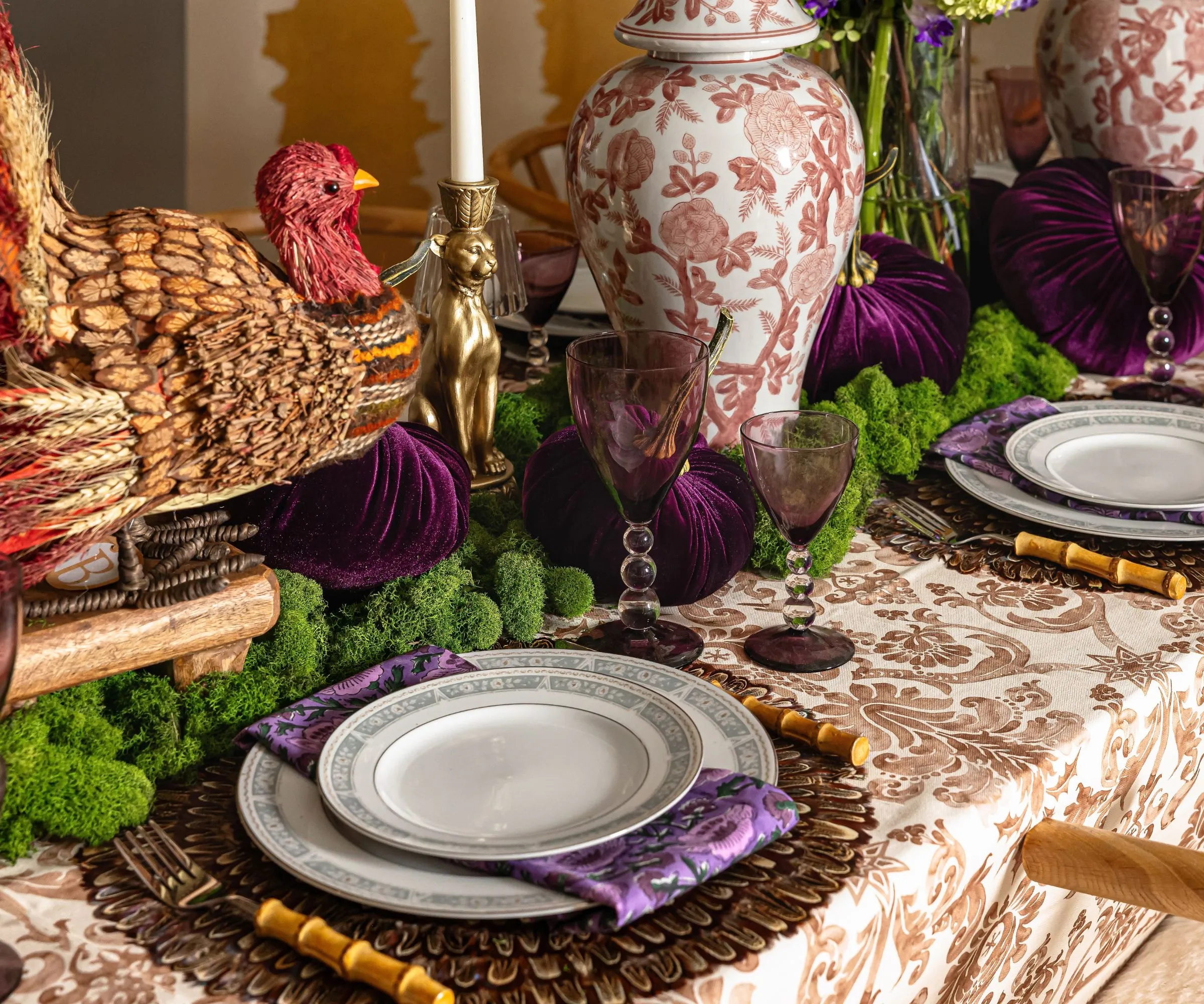 白と茶色の模様のテーブルクロス籐チャージャープレートと苔と生姜の瓶が入った大きな七面鳥のセンターピースを備えた感謝祭のテーブルスケープ' loading='lazy' title=