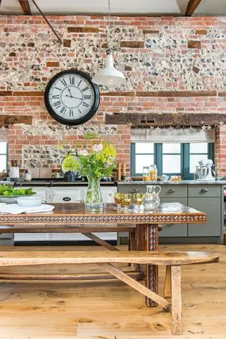 table de cuisine antique sculptée en bois sombre avec poutres apparentes, mur de briques aga et grande horloge