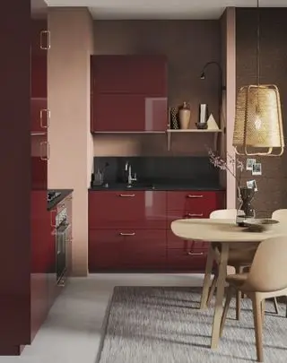 Une petite cuisine rouge avec des armoires brillantes, des murs roses et marron discrets et un mobilier en bois clair.