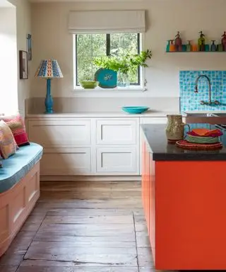 Une cuisine colorée beige, bleu pâle et rouge dans une maison de campagne du Sussex conçue par Kate Forman, avec un îlot de cuisine rouge orangé et du parquet.