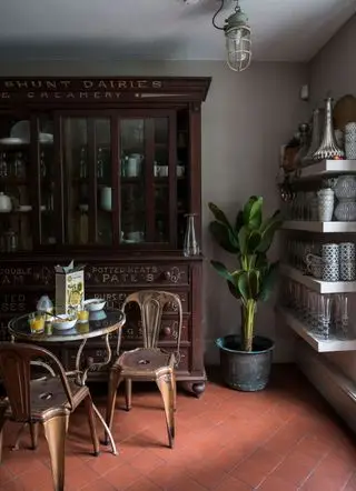 Une cuisine d'inspiration vintage avec du carrelage en terre cuite rouge, une table et des chaises en métal récupéré et un grand meuble ancien.