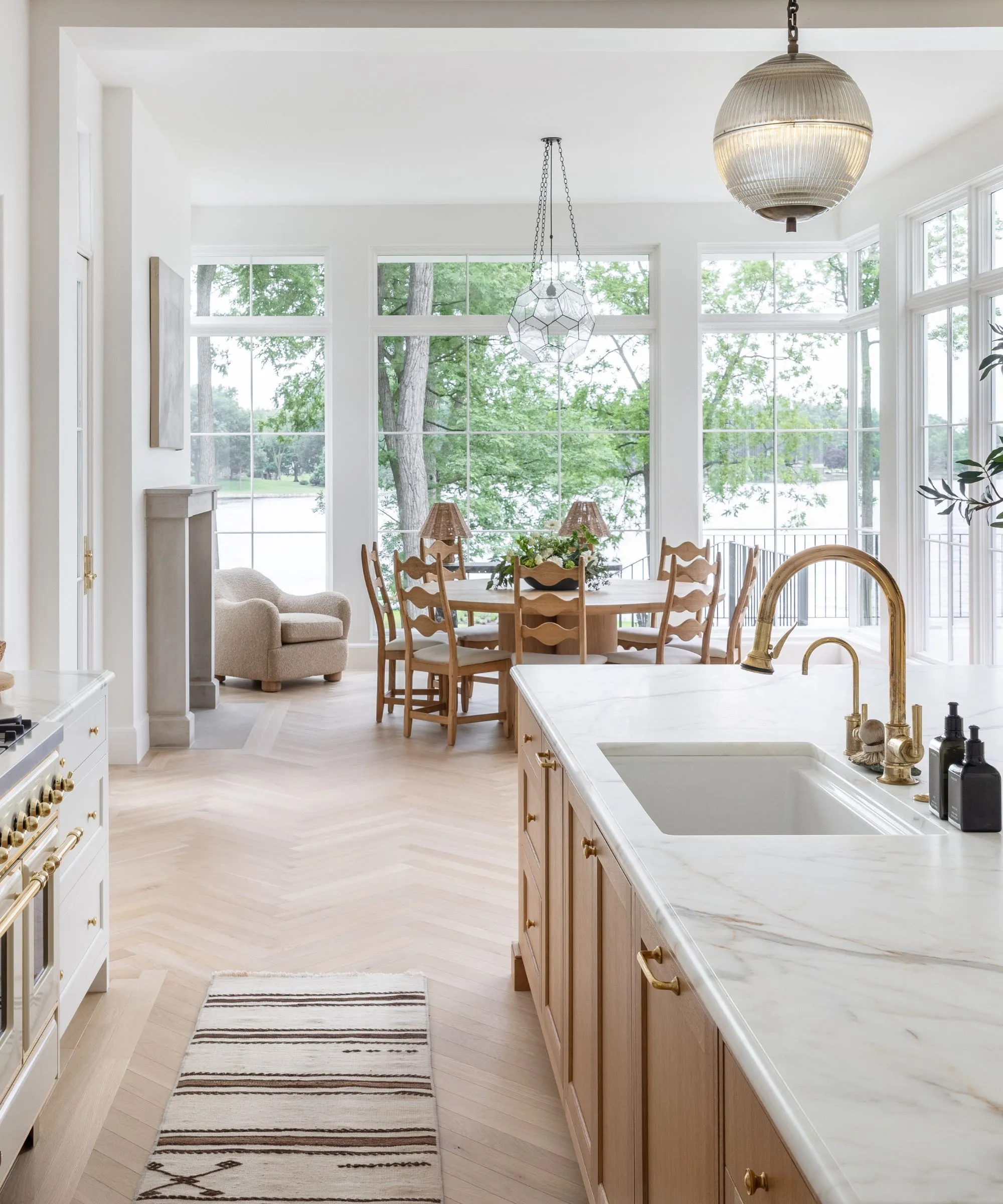 호수 전망을 감상할 수 있는 천장부터 바닥까지 내려오는 대형 창문으로 둘러싸인 끝에 식사 공간이 있는 목재 및 흰색 주방' loading='lazy' title=