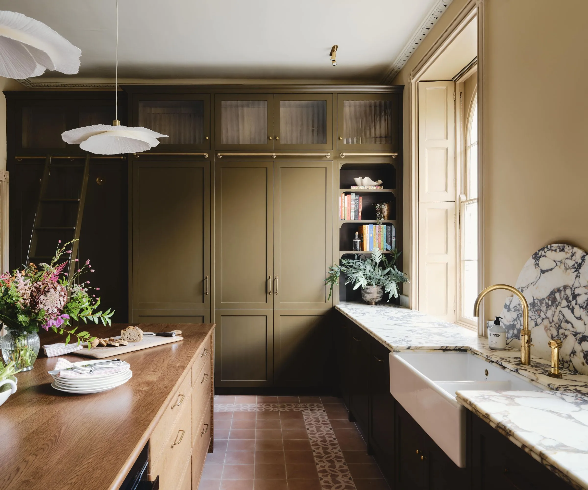 녹색 캐비닛, 목재 아일랜드 대리석 조리대 및 도자기 싱크대가 있는 따뜻한 시골 주방' loading='lazy' title=