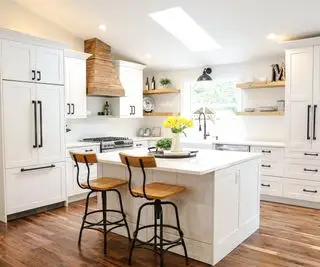 Cocina moderna de estilo rústico con gabinetes blancos, sillas tipo isla de madera y campana extractora.