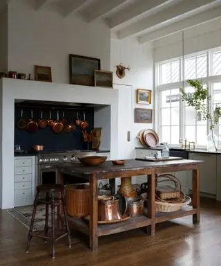 Cocina moderna de estilo rústico con techos altos, cocina tradicional y sartenes de cobre colgantes.