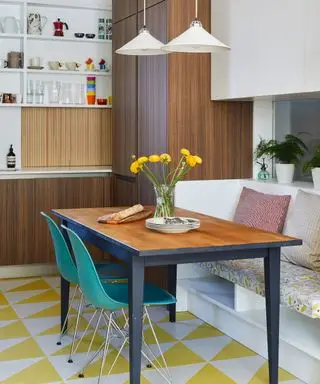 Cuisine-salle à manger avec sol en vinyle géométrique jaune et blanc, armoires et table à manger en bois foncé, banquette avec coussins, chaises de salle à manger bleues, suspensions basses