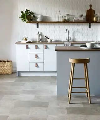 Cuisine avec sol en vinyle effet pierre grise, îlot de cuisine bleu-gris, armoires et comptoir de cuisine en bois blanc et foncé, étagères en bois foncé avec accessoires de cuisine