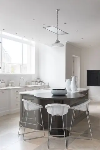 白い壁のキャビネットを備えたキッチン、はめ込みテーブルとバースツールを備えたグレーのアイランド、ニュートラルな床