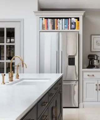 Primo piano dell'angolo della cucina con grande frigorifero doppio in alcova, scaffali e mobili circostanti, isola cucina con lavello, rubinetto in ottone