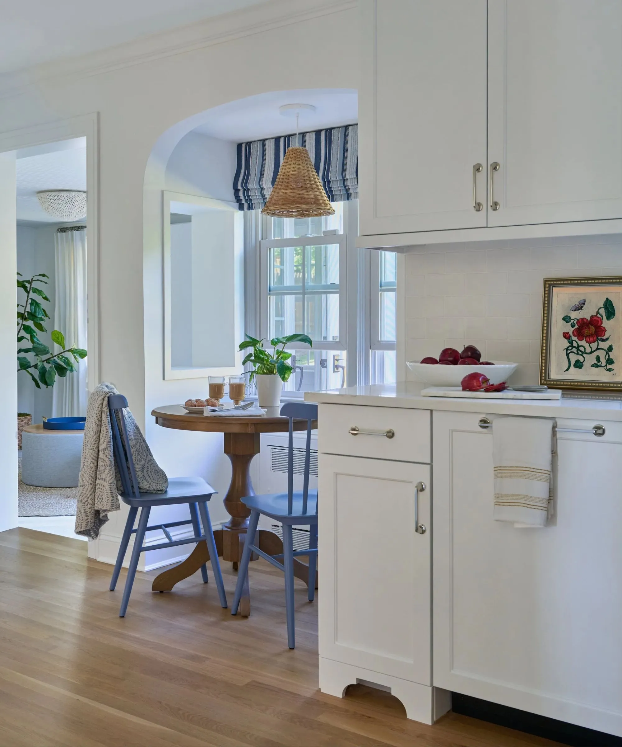 창문 옆에 식사 공간이 추가되고 파란색 줄무늬 창 처리가 적용된 흰색 주방 파란색 페인트 의자 나무 원형 테이블 패턴이 있는 던지기 및 등나무 펜던트 조명' loading='lazy' title=