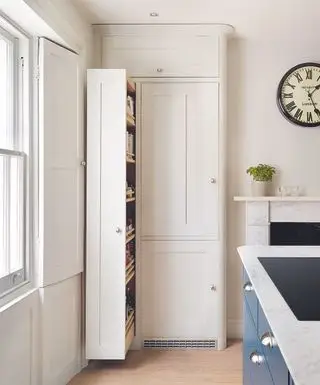 Un garde-manger étroit dans une cuisine blanche traditionnelle avec une grande horloge au mur