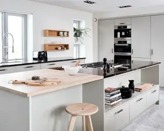 Cuisine moderne avec grand îlot de cuisine, comptoir en bois clair et pierre naturelle antique noire, armoires gris pâle et murs peints en blanc, bois clair, tabouret arrondi
