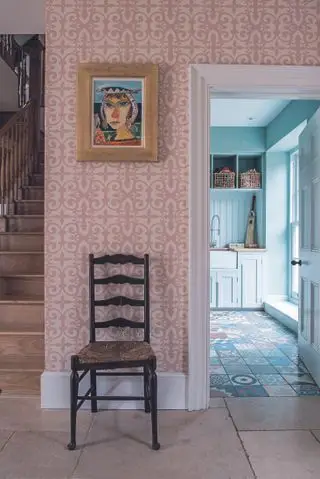 Un couloir avec un sol en pierre et du papier peint rose mène à une buanderie.