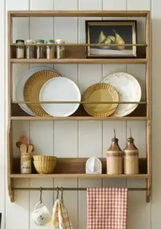Étagère murale peu profonde présentant des assiettes et des bocaux avec barrières en travers et porte-serviettes avec crochets en dessous