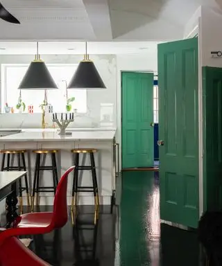 couleurs d'accents pour une cuisine blanche, cuisine monochromatique avec portes d'accent vert émeraude, sol noir, suspensions et tabourets de bar noirs et laiton, chaise rouge