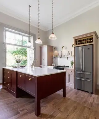 Cuisine moderne avec îlot de cuisine peint en rouge, comptoir en marbre, trois suspensions en verre et métal sur l'îlot, armoires peintes en rose, appliques murales sur étagère décorée