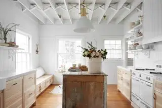 cuisine aux couleurs pâles et armoires en bois. Une île récupérée se dresse au centre