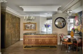 床から天井まで茶色のキャビネット、赤と金のアイランド、花柄の椅子が付いた円形テーブルを備えたキッチン、ダイニング、リビング スペース