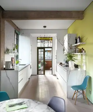 Un exemple d’idée d’aménagement de cuisine avec des armoires blanc brillant, un mur jaune et des chaises bleu sarcelle.