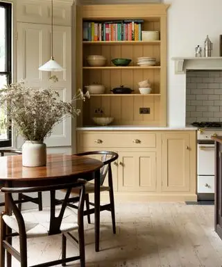 Cuisine shaker jaune avec une table ronde en bois et des chaises avec un grand vase de fleurs en son centre
