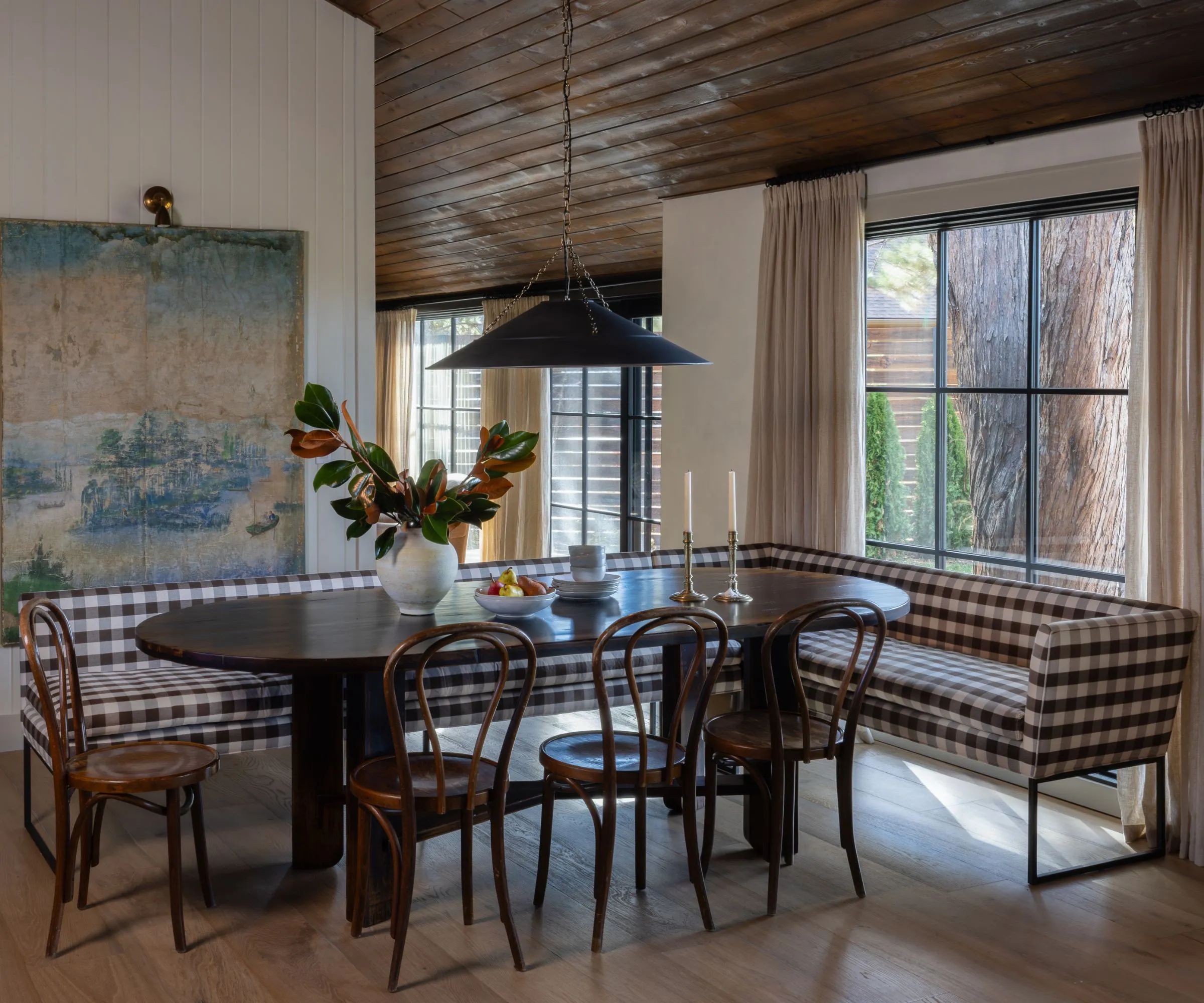 Pohled do kuchyně orámovaný dřevěnými dveřmi se středem na mramorovém ostrově a velkým klenutým oknem s výhledem na zelené stromy. Dvě bílá závěsná světla visí symetricky nad ostrovem' loading='lazy' title=