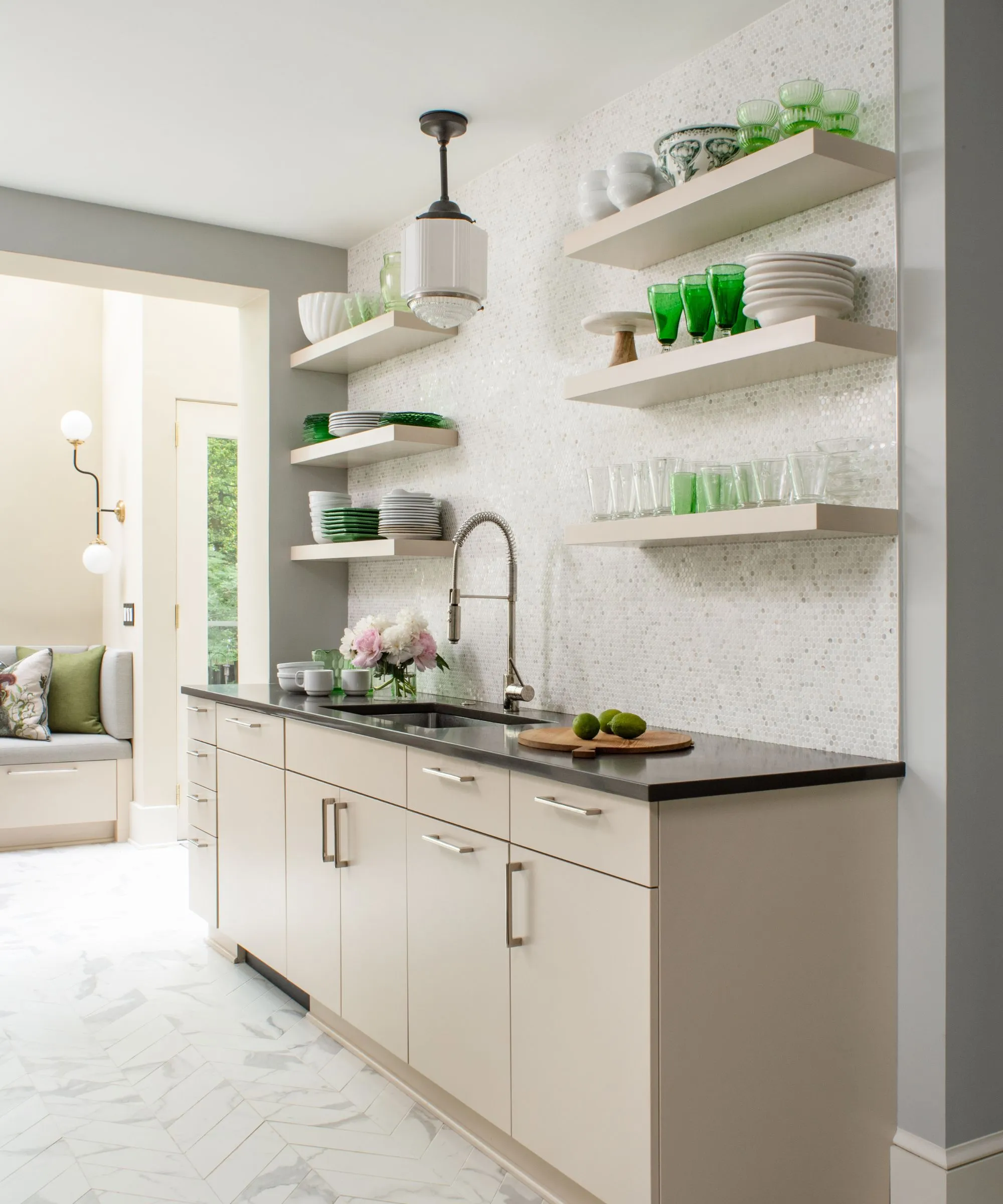 흰색 벽, 목재 캐비닛, 검은색 조리대, 녹색 유리 장식과 식기로 장식된 흰색 부동 벽 선반이 있는 중성적인 주방' loading='lazy' title=