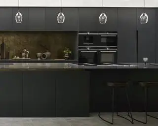 マットブラックのキャビネット、アイランドの石造りのワークトップ、真鍮のバックスプラッシュ、ペンダントライトを備えた黒のキッチンのアイデア