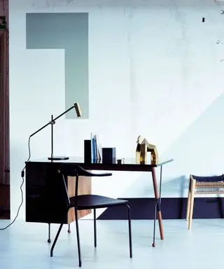 mesa preta e cadeira em uma sala em tons legais com lâmpada dourada