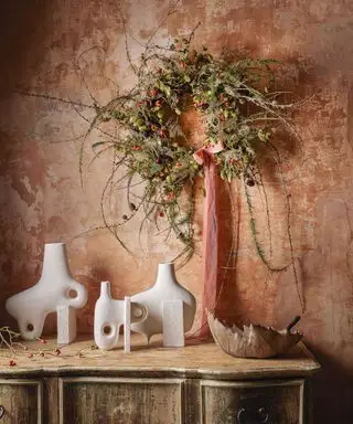 מזנון עם אגרטלים מודרניים מתחת זר ירוק ואדום עם סרט אדום תלוי על הקיר מעל.