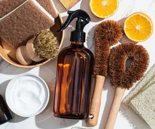 Une bouteille en verre ambré entourée de citrons, de bicarbonate de soude et de brosses à récurer