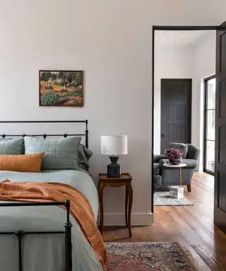 chambre avec lit en fonte avec jeté de couleur rouille et vue sur le salon aux murs blancs
