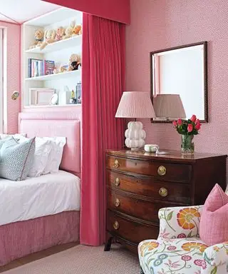 quarto rosa com cômoda de madeira e prateleiras abertas acima da cama