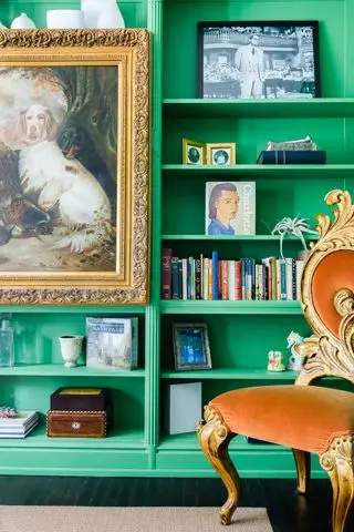 salon avec bibliothèque peinte en vert vif, chaise vintage rembourrée en velours, peinture vintage avec cadre doré orné